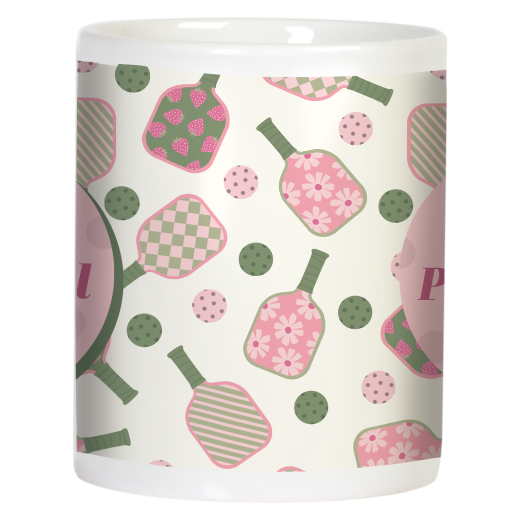 Side view of white ceramic pickleball mug, showcasing the continuous pink and green pattern of paddles and balls with polka dots, wrapped around the mug body.