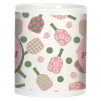 Side view of white ceramic pickleball mug, showcasing the continuous pink and green pattern of paddles and balls with polka dots, wrapped around the mug body.