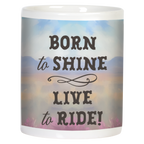 Back view of a white ceramic mug displaying the inspirational text "BORN to SHINE LIVE to RIDE!" in dark brown script over a soft watercolor background with distant mountains and a serene sunset sky.