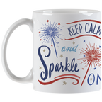 Full view of a white ceramic coffee mug with an encouraging 'Keep Calm and Sparkle ON' message, decorative red and blue sparklers, and stars, with the handle visible.