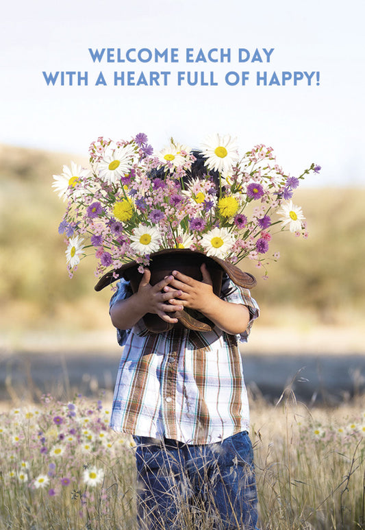 A child hiding behind a hat overflowing with white, yellow, and purple wildflowers and daisies with text 'WELCOME EACH DAY WITH A HEART FULL OF HAPPY!'