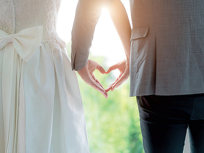 Newlywed couple's hands form a heart, bathed in warm sunlight, symbolizing love and unity.