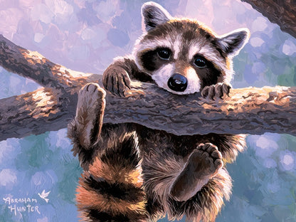 An adorable baby raccoon playfully hangs from a tree branch, looking directly at the viewer with big, curious eyes.