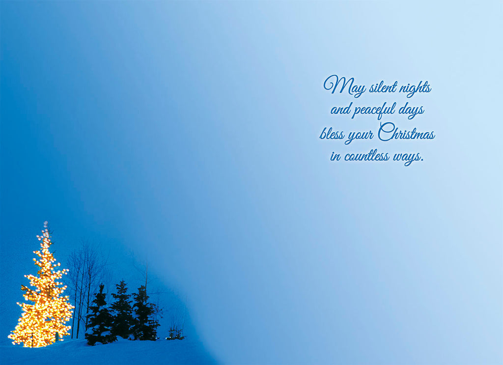 Inside a heartfelt religious greeting card with a gentle blue gradient background and a small glowing evergreen tree in a snowy setting. The card's interior message reads 'May silent nights and peaceful days bless your Christmas in countless ways,' conveying peaceful holiday blessings.