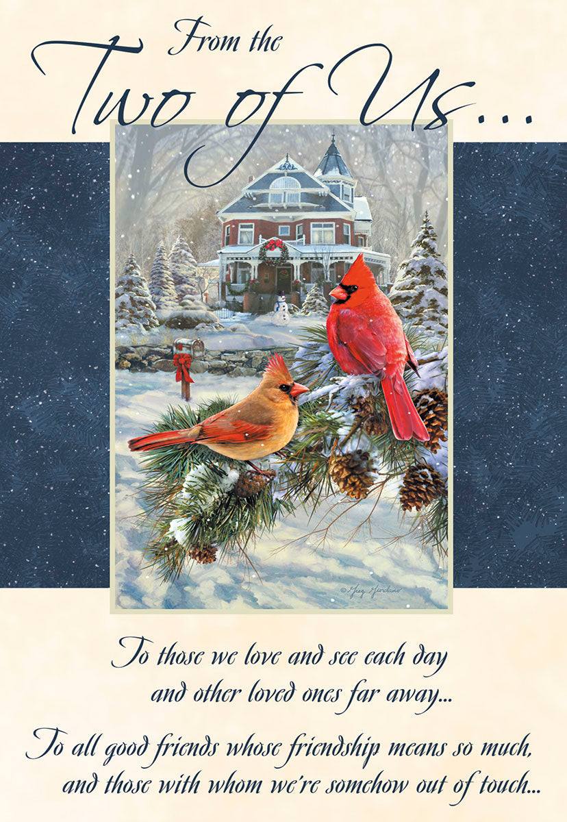 Front of a winter greeting card featuring two vibrant red cardinals perched on a snow-dusted pine branch in front of a festive, elegant Victorian house, with 'From the Two of Us...' script.