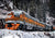 orange train engine traveling through snowy mountains