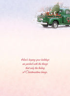 Interior of a holiday greeting card with elegant red script reading 'Here's hoping your holidays are packed with the things that only the feeling of Christmastime brings.' against a soft, snowy background with a subtle festive truck in the distance.