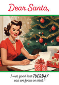 Retro style greeting card featuring a woman in a red dress writing a letter to Santa beside a decorated tree and gifts, with the text 'Dear Santa, I was good last TUESDAY can we focus on that?'