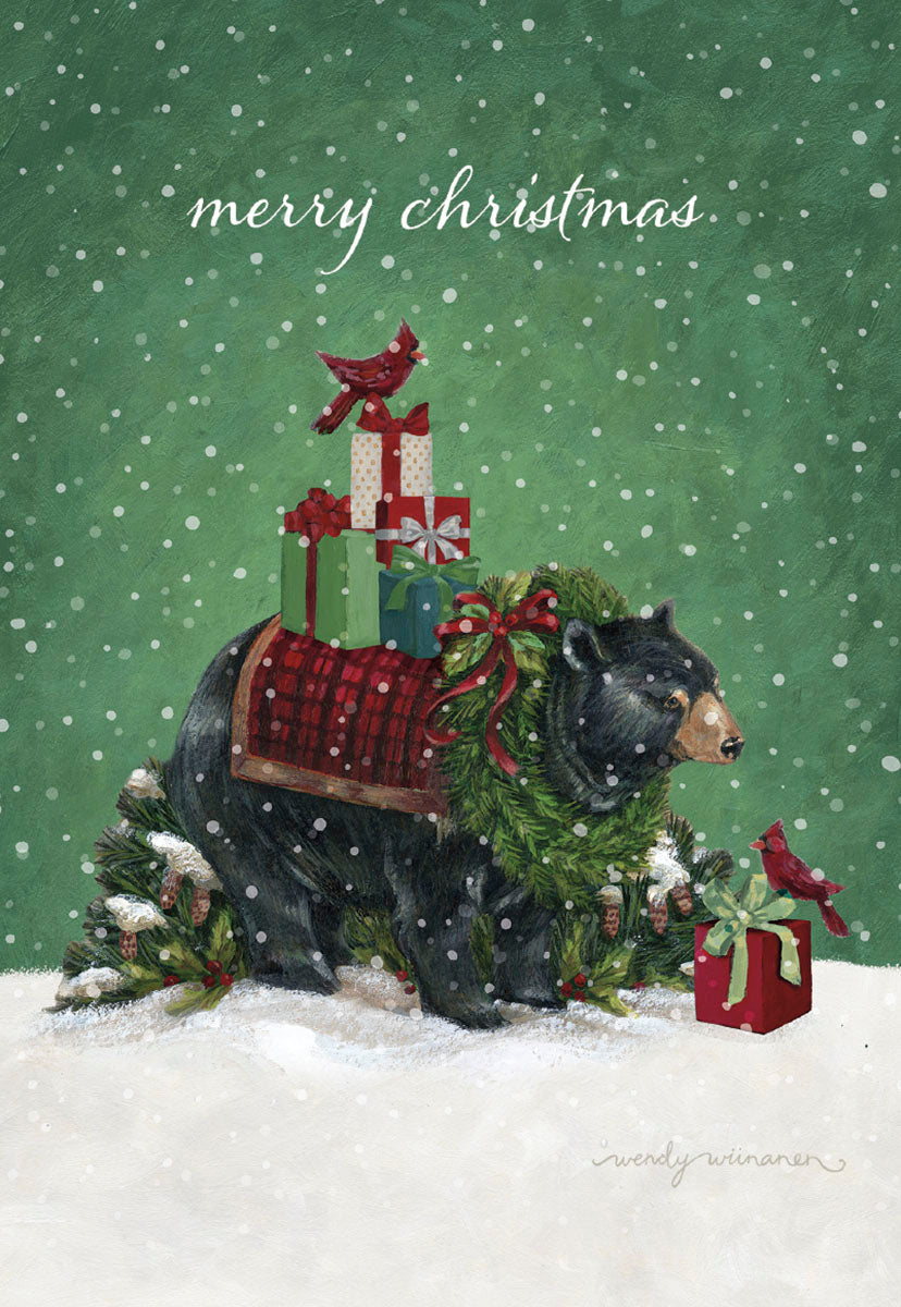 Front of a festive greeting card featuring a majestic black bear adorned with a green wreath and red tartan saddle blanket, carrying a stack of beautifully wrapped holiday presents. A bright red cardinal perches on the gifts, with falling snow against a vibrant green background, conveying a warm winter wonderland scene. The words 'merry christmas' are subtly displayed at the top.