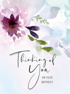 Front of a watercolor floral birthday card with soft purple, pink, and teal flowers. The card reads 'Thinking of You ON YOUR BIRTHDAY' in elegant script.