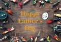 Flat lay of vintage fishing lures, bobbers, and reels framing 'Happy Father's Day' text on a rustic wood background, perfect for outdoorsy dads.