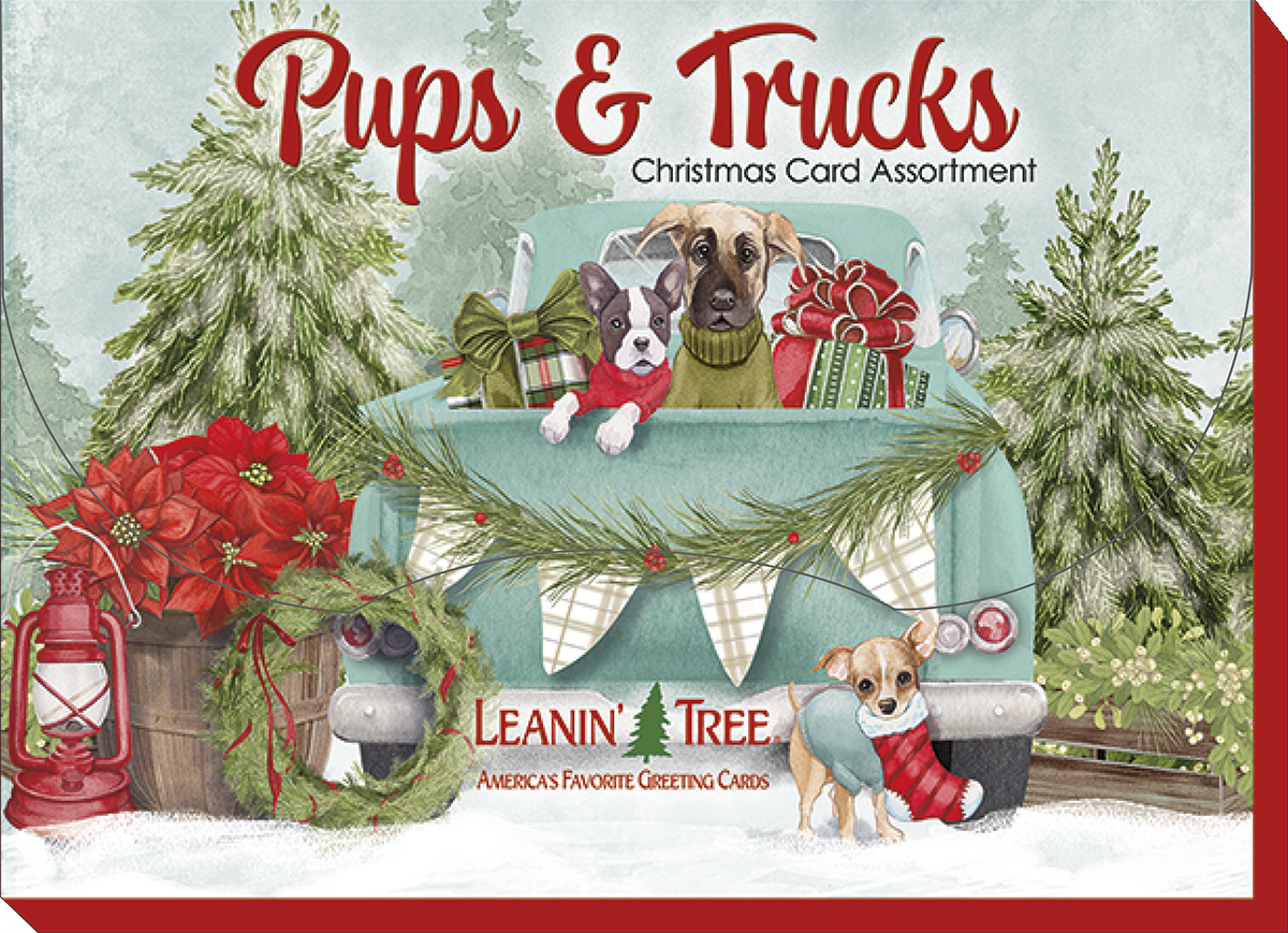Leanin' Tree Pups & Trucks Christmas Card Assortment box cover with two dogs in a light blue vintage pickup truck adorned with holiday garland and presents, surrounded by snowy evergreens.