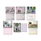 Ten different greeting card fronts from the assortment displayed with their blank interior sides, highlighting the variety of designs such as a bicycle, lavender, a coffee shop, and a farmers market.