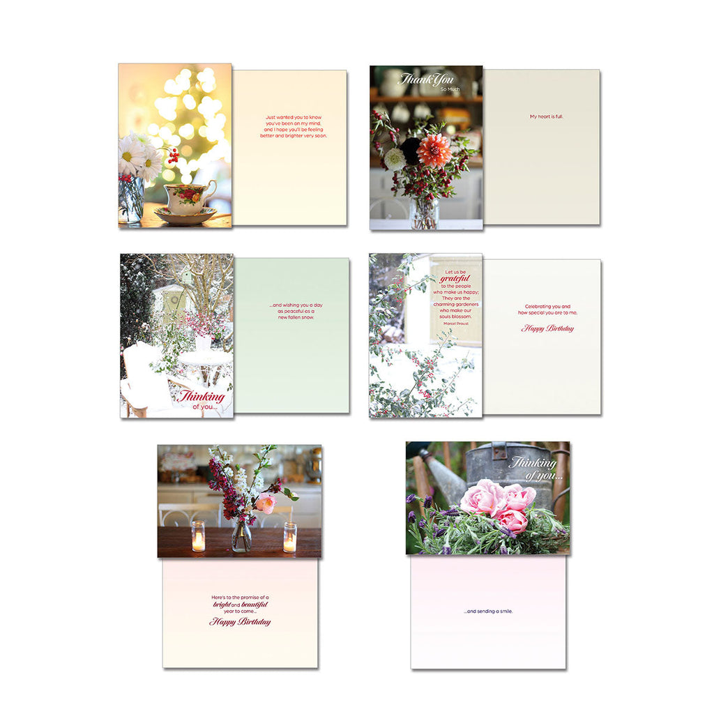 Collection of Leanin' Tree greeting cards showing front and inside designs: 'Thinking of You' with bokeh lights, 'Let us be grateful' with a snowy scene, 'Thank You' with a floral arrangement, 'Happy Birthday' with blooming flowers, 'Thinking of You' with lit candles, and 'Thinking of You' with roses in a watering can, highlighting emotional versatility.