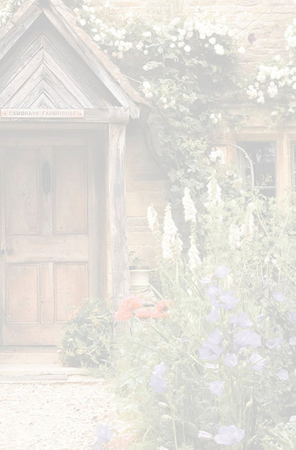 Muted, soft view of a rustic wooden door of a charming stone cottage with a small porch and blooming garden flowers.