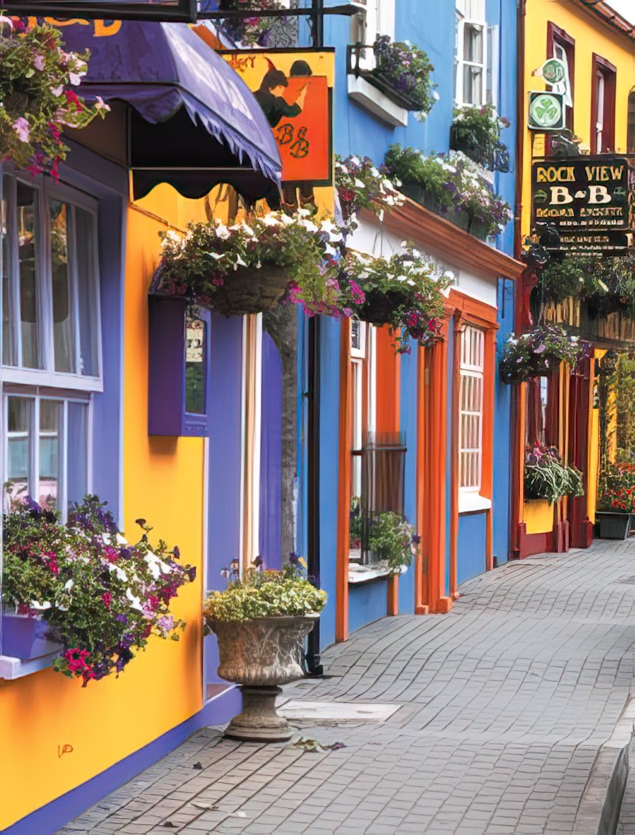 Brightly colored houses in yellow, blue, and purple line a narrow European street, featuring charming window boxes.
