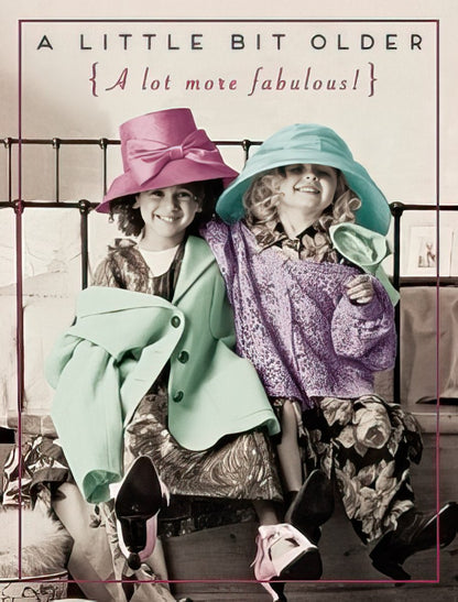 Front of a birthday card featuring two smiling girls in oversized hats and coats with text 'A Little Bit Older {A lot more fabulous!}'.