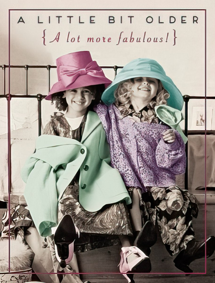 Two joyful young girls in oversized colorful hats and coats, playing dress-up, with the text 'A Little Bit Older {A lot more fabulous!}' on a playful greeting card. Ideal for a child's birthday celebration.