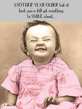 Funny birthday card featuring a baby in a pink dress making a hilarious scrunched-up face, with text 'ANOTHER YEAR OLDER but at least you've still got something to SMILE about,' perfect for a friend's milestone celebration.