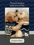 Front of a romantic anniversary greeting card featuring two golden retriever puppies snuggling under a patterned blanket. Text reads 'The best thing to hold on to in life... is each other.' on a dark blue chevron background, perfect for a spouse or partner.