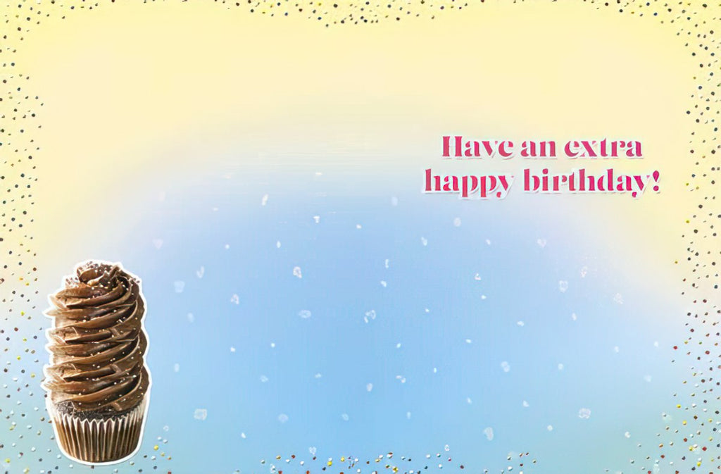 Interior view of a festive birthday greeting card showing a small, appetizing chocolate cupcake with sprinkles on the left. The right side features the celebratory message 'Have an extra happy birthday!' in bold pink text, all against a blurred yellow and blue confetti background, indicating a joyous occasion.