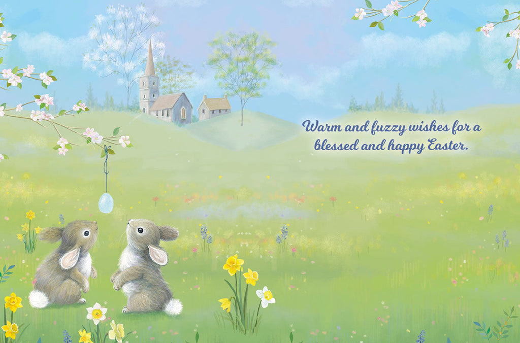 Inside of a greeting card showing two cute bunnies in a spring field with a church, displaying the message 'Warm and fuzzy wishes for a blessed and happy Easter,' ideal for religious well wishes and seasonal greetings.
