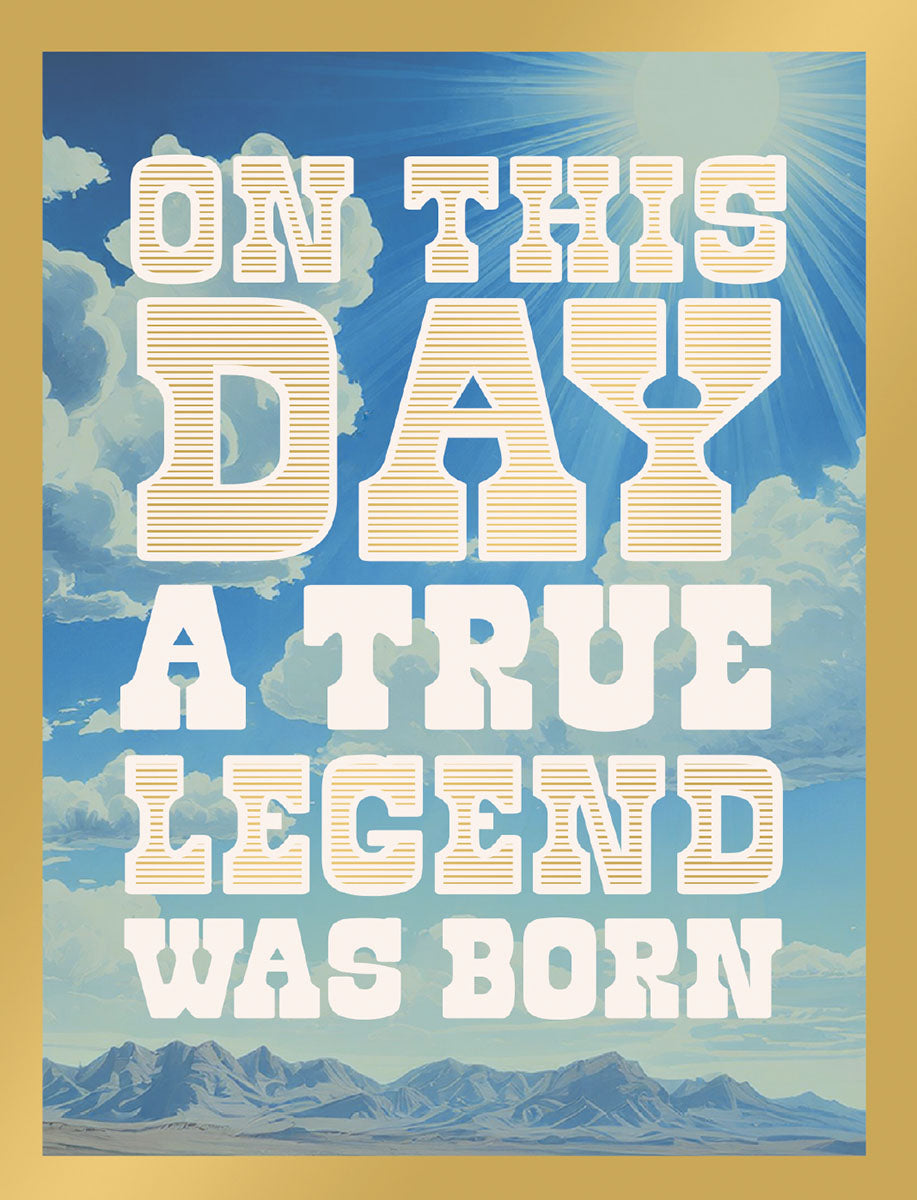 Front view of an inspiring greeting card featuring 'ON THIS DAY A TRUE LEGEND WAS BORN' in gold and white text, set against a vibrant blue sky with clouds and distant mountains.