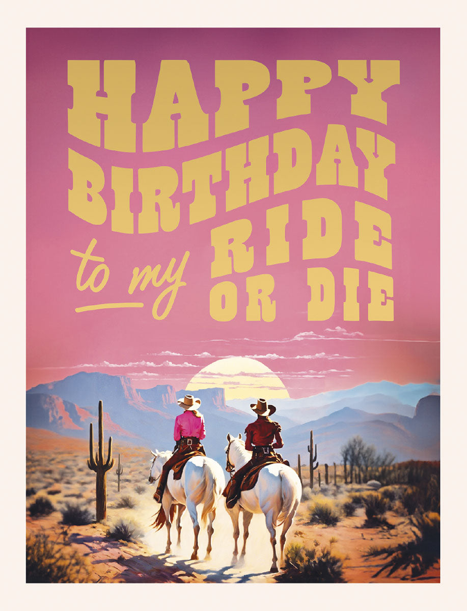 Front of a vibrant pink and orange sunset birthday card featuring two figures on horseback in a desert landscape with saguaro cacti, bold text reads 'HAPPY BIRTHDAY to my RIDE OR DIE'.