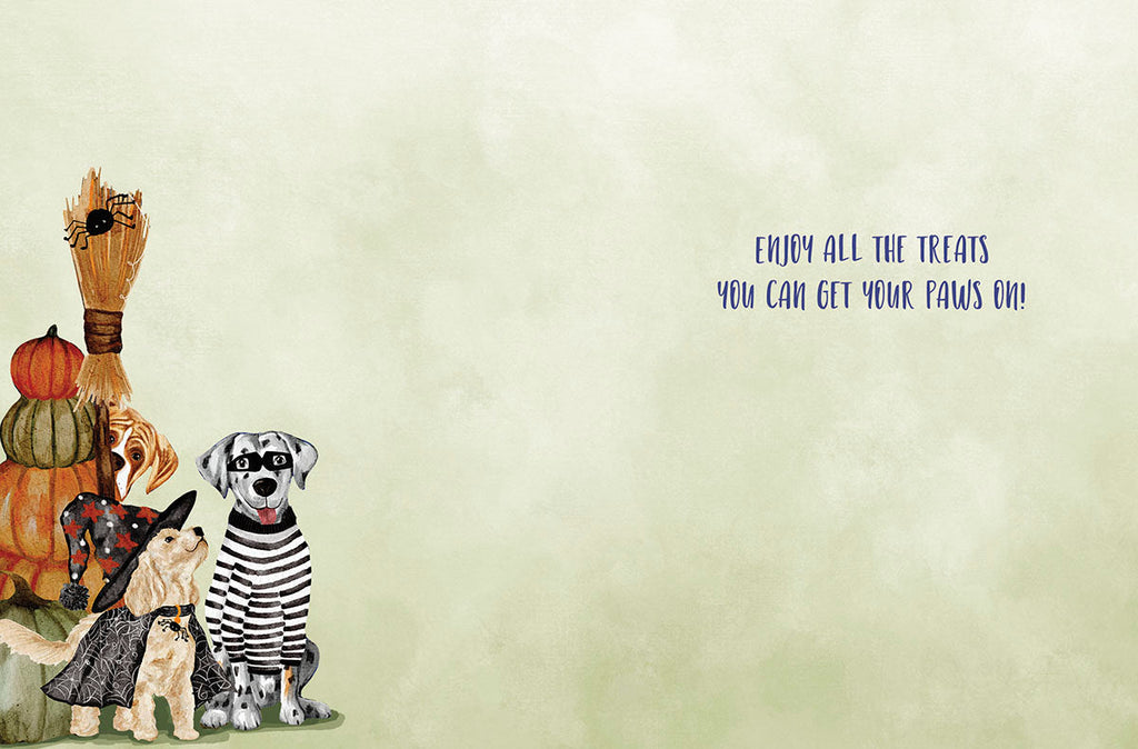 The inside of a greeting card featuring three cute dogs in costumes on the left, alongside pumpkins and a broom. The right side has ample space for a personal message, with the printed text "ENJOY ALL THE TREATS YOU CAN GET YOUR PAWS ON!" on a light green background, continuing the cheerful spooky theme.