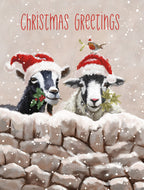 Front of a cute winter greeting card featuring a black goat and white sheep wearing red Santa hats, peeking over a snowy stone wall. Both animals hold holly and mistletoe sprigs. A small robin with mistletoe perches on the sheep's hat. Gentle snow falls, creating a whimsical festive scene.