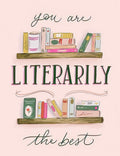 Front of a humorous birthday greeting card featuring two whimsical wooden bookshelves filled with colorful books and the clever pun 'you are LITERARILY the best' in elegant script and bold green lettering on a soft pink background, perfect for a book lover.