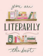 Front of a humorous birthday greeting card featuring two whimsical wooden bookshelves filled with colorful books and the clever pun 'you are LITERARILY the best' in elegant script and bold green lettering on a soft pink background, perfect for a book lover.