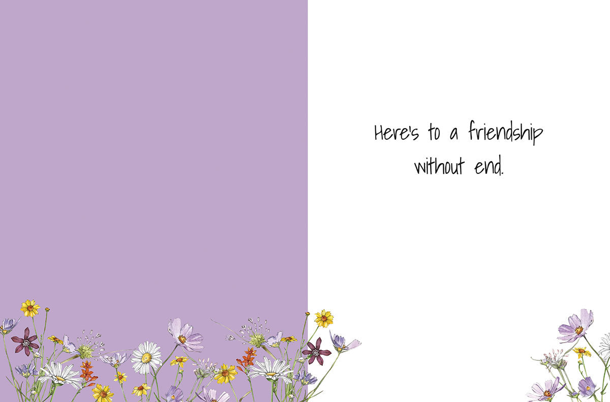 Inside of a heartfelt greeting card for friends, displaying a soft purple left panel and a white right panel. At the bottom, a scattering of colorful wildflowers. The message on the white panel reads: 'Here's to a friendship without end.'