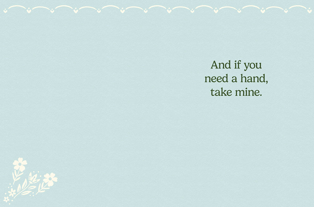 Inside of a light blue greeting card for friends, displaying a simple heartfelt message 'And if you need a hand, take mine.' with a subtle white floral sprig in the bottom left corner.