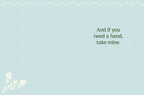 Inside of a light blue greeting card for friends, displaying a simple heartfelt message 'And if you need a hand, take mine.' with a subtle white floral sprig in the bottom left corner.