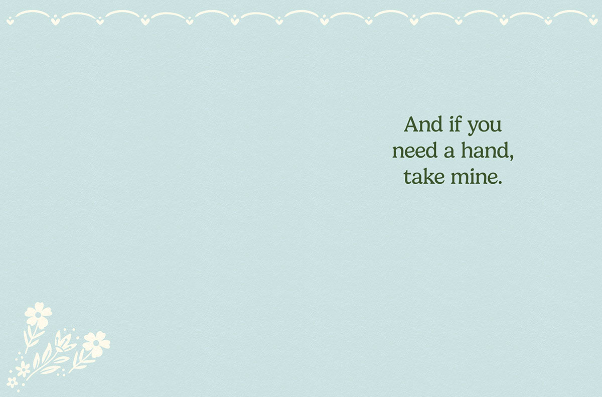 Inside of a light blue greeting card for friends, displaying a simple heartfelt message 'And if you need a hand, take mine.' with a subtle white floral sprig in the bottom left corner.