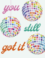 Front of a vibrant, funny birthday greeting card featuring three colorful disco balls and the playful message 'you still got it' in pink, green, and orange typography on a light grey background. Perfect for a friend's special day.