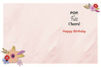 Inside of a cheerful greeting card with 'POP. Fizz. Cheers! Happy Birthday' text, accompanied by delicate floral accents on a soft pink background.