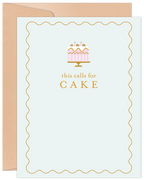 Elegant birthday greeting card featuring a pink and gold cake illustration with text 'this calls for CAKE' on a light blue background with a gold wavy border, accompanied by a kraft envelope.