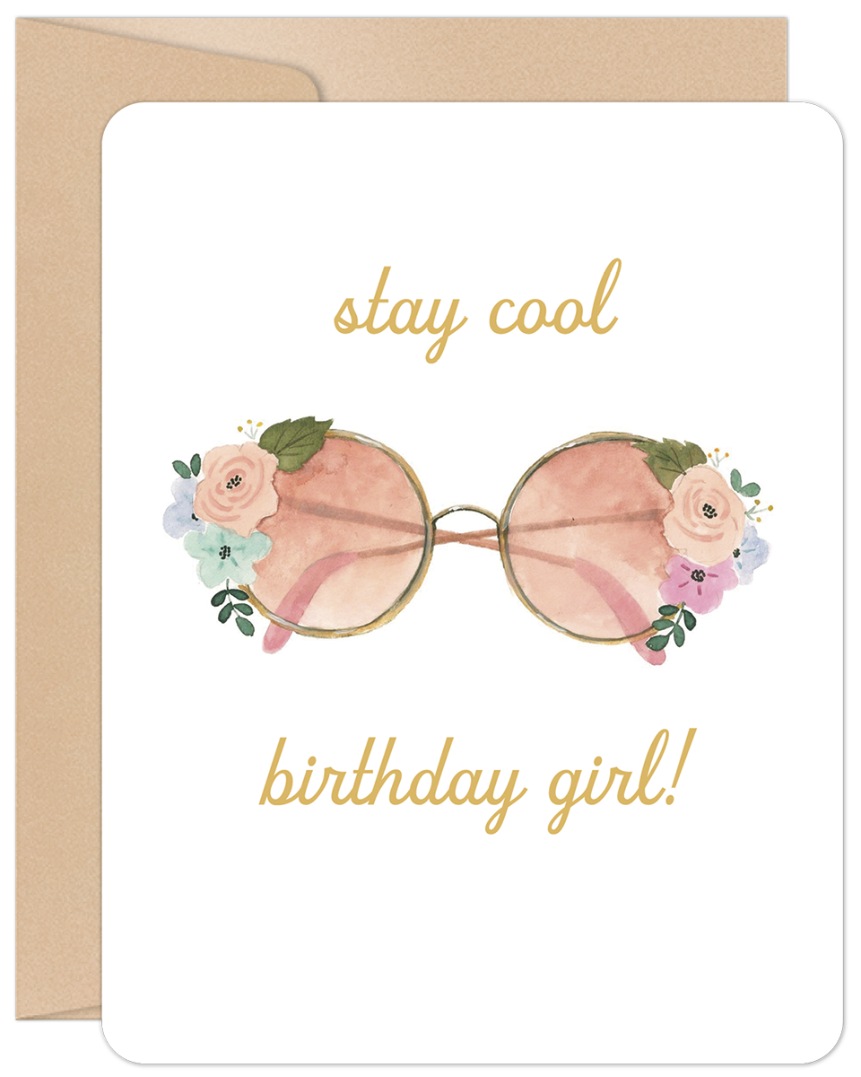 Front of a white birthday greeting card featuring a watercolor illustration of pink-lensed round sunglasses adorned with soft pink, blue, and green floral accents. Above the sunglasses, the text reads "stay cool" and below, "birthday girl!" in elegant gold script. A brown kraft paper envelope is visible behind the card.