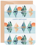 Front view of a lighthearted birthday greeting card featuring a repeating pattern of colorful sailboats on reflective blue water with orange sunsets, accompanied by a kraft paper envelope.