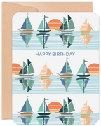 Front view of a lighthearted birthday greeting card featuring a repeating pattern of colorful sailboats on reflective blue water with orange sunsets, accompanied by a kraft paper envelope.