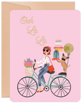 Stylish woman on a vintage bicycle with flowers, a pug, gifts, and 'Ooh La La' text on a pink lighthearted greeting card, ideal for Her.