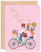 Stylish woman on a vintage bicycle with flowers, a pug, gifts, and 'Ooh La La' text on a pink lighthearted greeting card, ideal for Her.