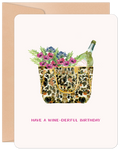 Watercolor illustration of a leopard print tote bag overflowing with vibrant purple and pink flowers, greenery, and a bottle of sparkling wine. The text 'HAVE A WINE-DERFUL BIRTHDAY' is printed below, set against a light background with a kraft brown envelope peeking out.