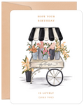 Watercolor illustration greeting card featuring a charming flower cart with vibrant pink, orange, and yellow blooms under a black and white striped awning. Elegant text reads 'HOPE YOUR BIRTHDAY IS LOVELY (LIKE YOU)'. Perfect floral card for a special celebration.