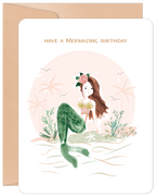 Charming mermaid greeting card for kids featuring a whimsical illustration of a brown-haired mermaid with a floral crown and green tail, sitting on a sandy beach with palm trees, wishing 'Have a Mermazing Birthday'.