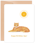 Greeting card featuring a stylized orange tiger lying under a bright yellow sun, with the cheerful message 'happy birthday, tiger' on a white background, partially revealing a kraft envelope.