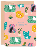 Front of a cute birthday greeting card featuring an array of white, black, and ginger cats lounging on colorful floral and patterned armchairs and sofas, surrounded by potted plants on a light pink background. The text 'HAPPY BIRTHDAY' is centrally placed.