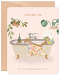 Front view of a light pink greeting card for her, featuring a woman with white hair relaxing in a bubble bath with cucumber slices on her eyes, champagne, and houseplants. Text reads 'STAYING IN... IT'S THE NEW GOING OUT!'